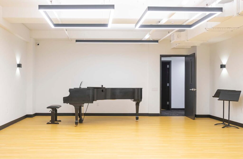 Black Grand Piano with Bench in a rehearsal studio with wooden floor and music stands